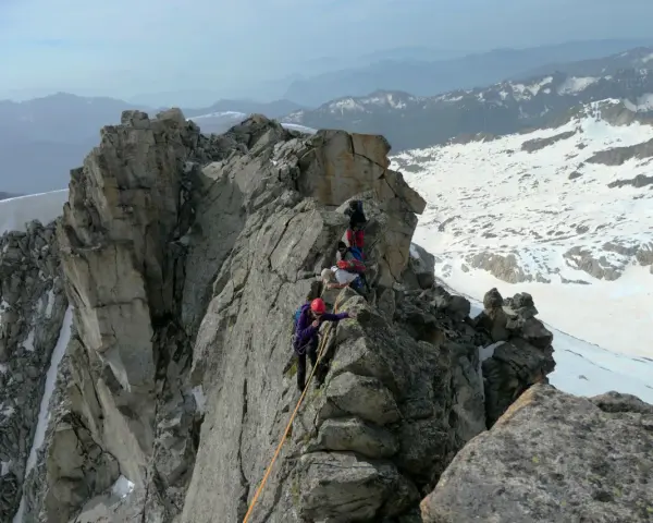 Alpinisti in cordata affrontano un crinale roccioso innevato, con la **cima Presanella** sullo sfondo.