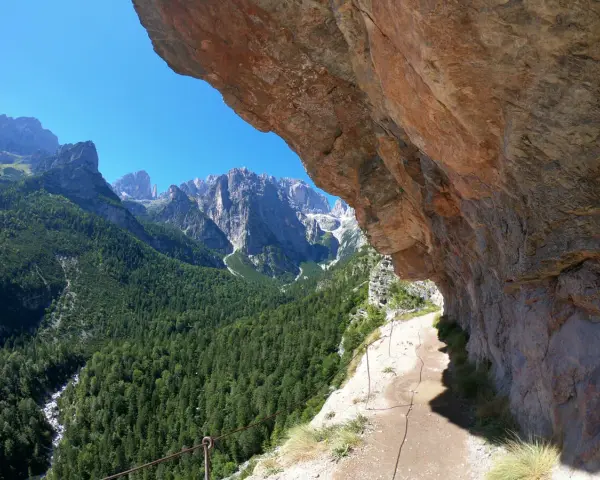 Sentieri panoramici vicino al Lago di Molveno, con un sentiero che costeggia una parete rocciosa e una vista mozzafiato sulle montagne e una cascata in lontananza.