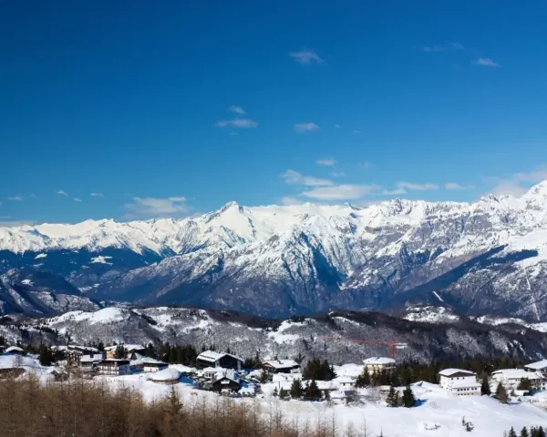 Paesaggio invernale con case innevate e montagne maestose sullo sfondo, un incantevole scenario al Passo Bondone.