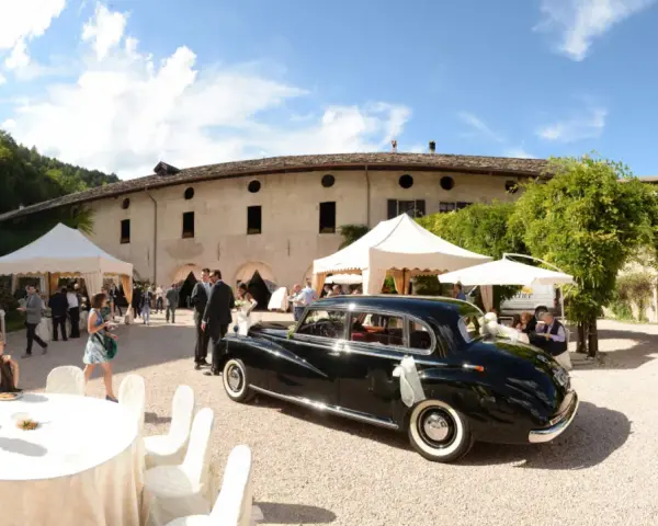 Matrimonio a Caldonazzo centro storico: auto d'epoca nera, tavoli allestiti, ospiti e un campanile sullo sfondo.