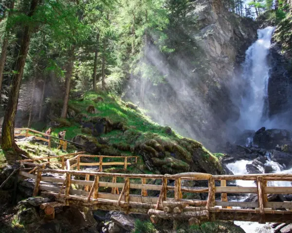Sentiero in legno conduce alle maestose cascate Val di Sole, immerse in un bosco rigoglioso.