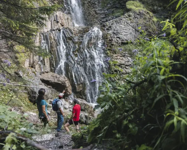 Escursionisti ammirano le spettacolari cascate schiavaneis, immerse nel verde e circondate da rocce basaltiche.