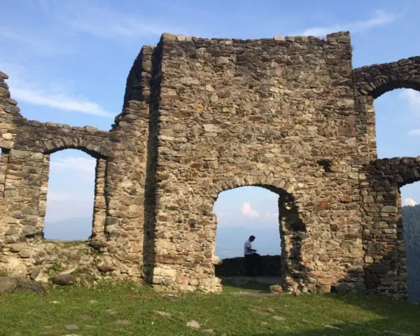 Rovine del castello di Altaguardia, con un uomo seduto che guarda il panorama.