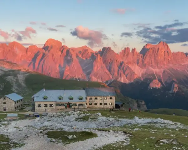 Rifugio sul **Monte Catinaccio** illuminato dal tramonto, con le vette rocciose che si tingono di rosa.