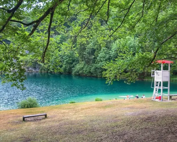Rilassante **lago Lamar** con acque turchesi, bagnanti e torretta di salvataggio sotto alberi verdi.