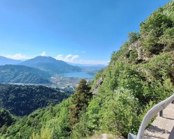 Vista panoramica dal Monte Vezzena con lago azzurro e montagne sullo sfondo. Strada con galleria scavata nella roccia.