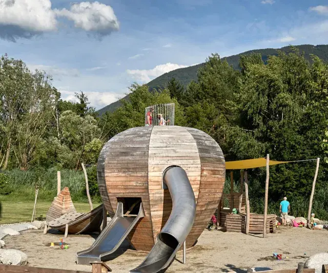 Un colorato parco giochi Trentino con una struttura a forma di sfera in legno, scivoli e bambini che giocano.