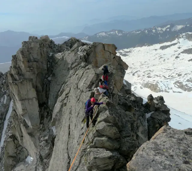 Alpinisti in cordata affrontano un crinale roccioso innevato, con la **cima Presanella** sullo sfondo.