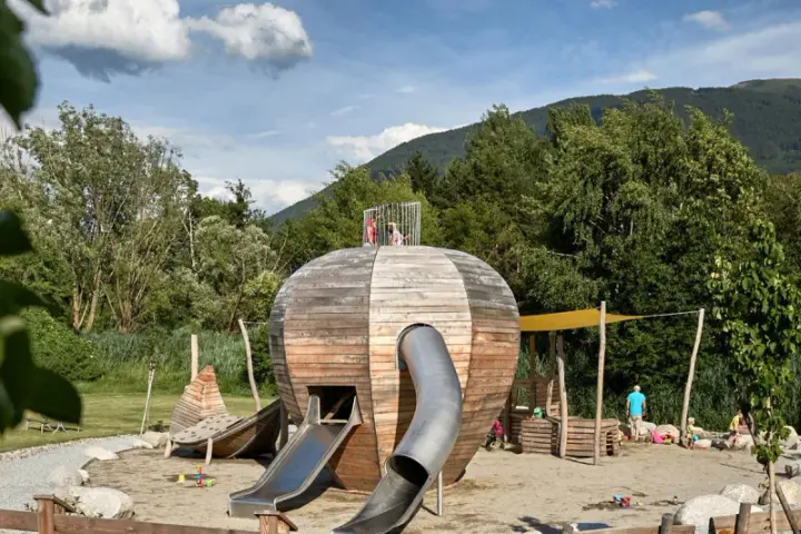 Un colorato parco giochi Trentino con una struttura a forma di sfera in legno, scivoli e bambini che giocano.