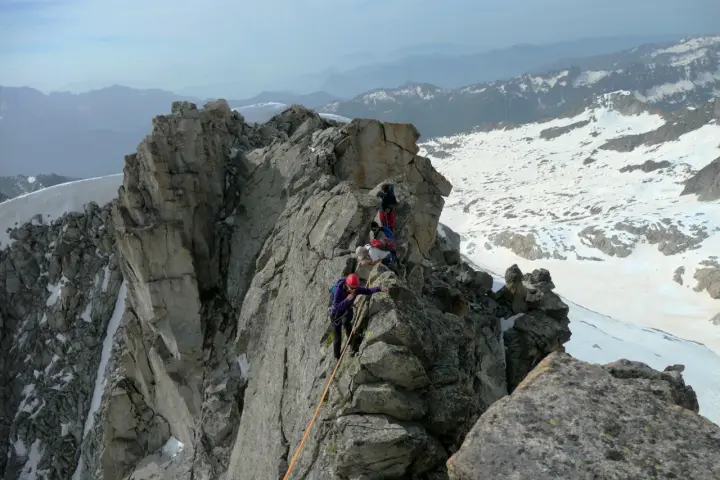 Alpinisti in cordata affrontano un crinale roccioso innevato, con la **cima Presanella** sullo sfondo.