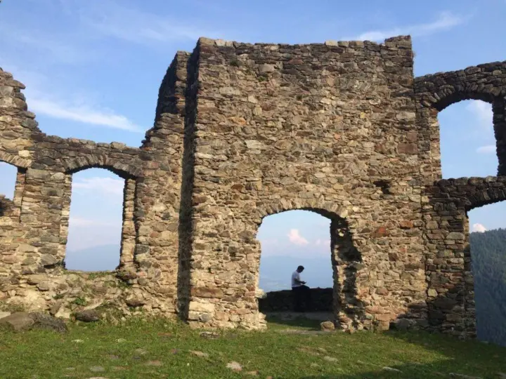 Rovine del castello di Altaguardia, con un uomo seduto che guarda il panorama.
