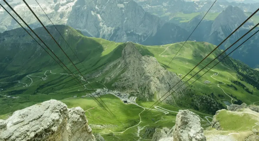 Vista mozzafiato da Canazei al Passo Sella, con funivia che attraversa verdi pendii e imponenti vette dolomitiche.
