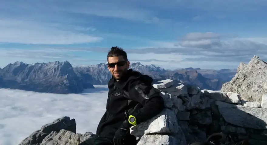 Uomo in vetta con abbigliamento tecnico, ideale per capire come vestirsi in montagna a settembre. Paesaggio alpino mozzafiato.