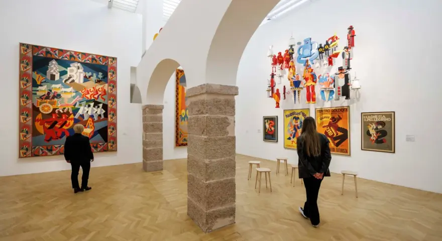Un visitatore ammira un arazzo colorato e installazioni futuristiche al muse rovereto.