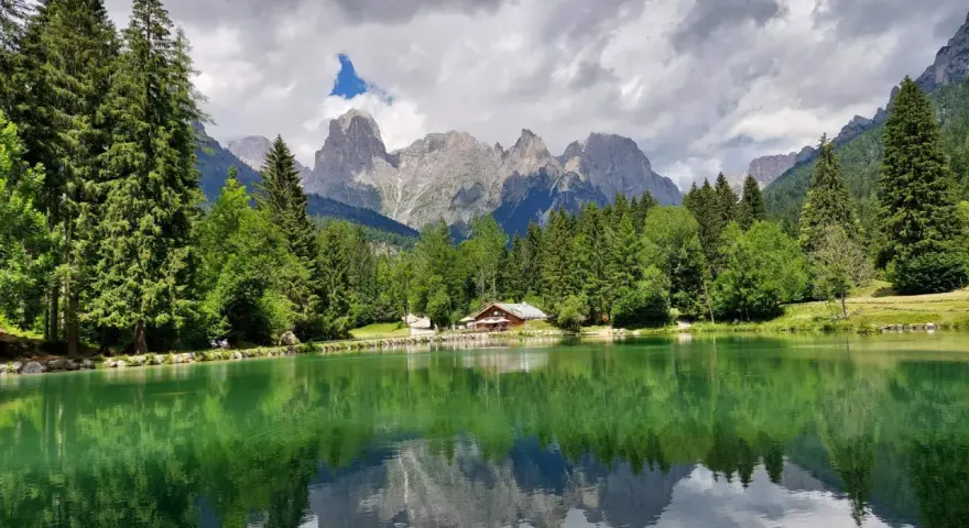 Riflessi alpini sul lago di Passo Cereda. Montagne imponenti e boschi verdi incorniciano un tranquillo specchio d'acqua.