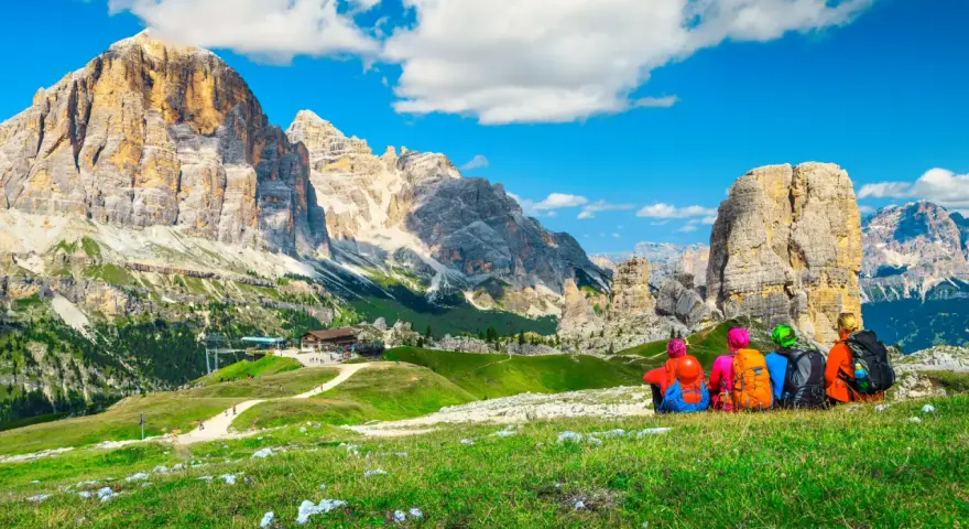 Quattro escursionisti ammirano le maestose Dolomiti Trentino Alto Adige, con cime imponenti e un cielo azzurro.