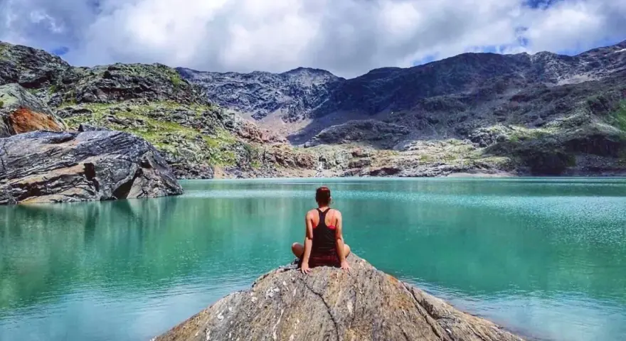 Donna seduta su una roccia ammira il **lago del Carest** con le montagne sullo sfondo.