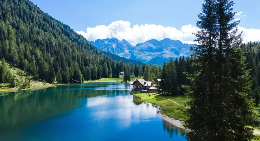 Incantevole lago alpino vicino a Madonna di Campiglio, con boschi rigogliosi, montagne maestose e un rifugio accogliente.