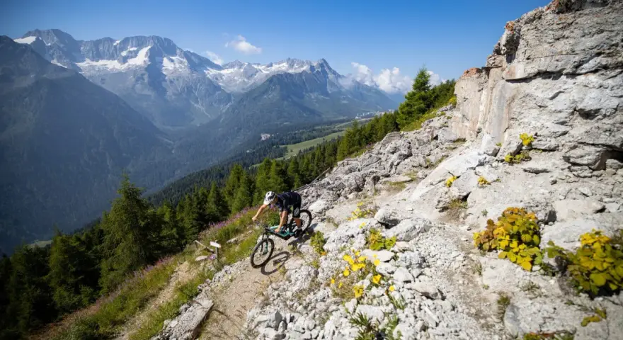 Ciclista in discesa su sentiero roccioso, con montagne innevate sullo sfondo, durante il giro dei forti tonale.