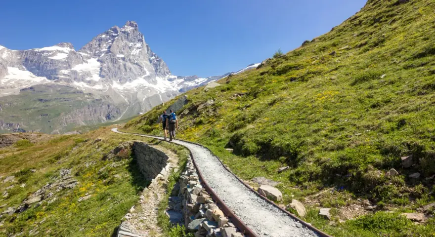 Due escursionisti affrontano un sentiero panoramico, con il Cervino innevato sullo sfondo, durante un **trekking due giorni Dolomiti**.
