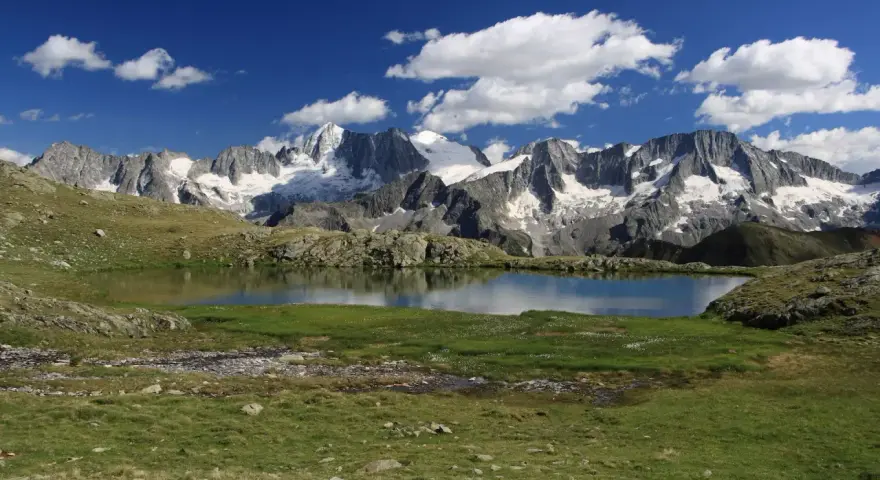 Laghi Val di Sole raggiungibili in auto: specchio d'acqua alpino con montagne innevate sullo sfondo e cielo azzurro con nuvole bianche.