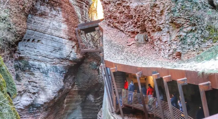 Persone percorrono una passerella metallica lungo le pareti rocciose di un canyon, vicino al Ponte dell'Orrido.