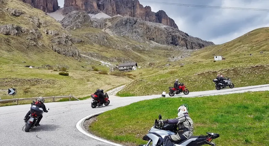Motociclisti affrontano tornanti sui **Dolomiti passi**, con imponenti vette sullo sfondo.