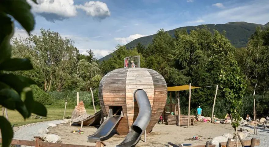 Un colorato parco giochi Trentino con una struttura a forma di sfera in legno, scivoli e bambini che giocano.