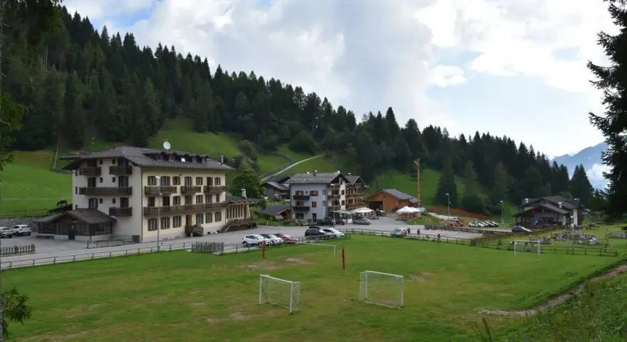 Edifici alpini e un campo da calcio con porte, immersi nel verde e circondati da boschi. La **passo Cereda altitudine** offre uno scenario incantevole.