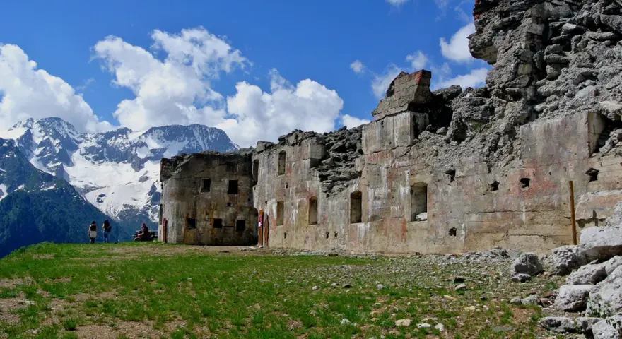 Rovine del forte Zaccarana, con montagne innevate sullo sfondo e cielo azzurro con nuvole bianche.