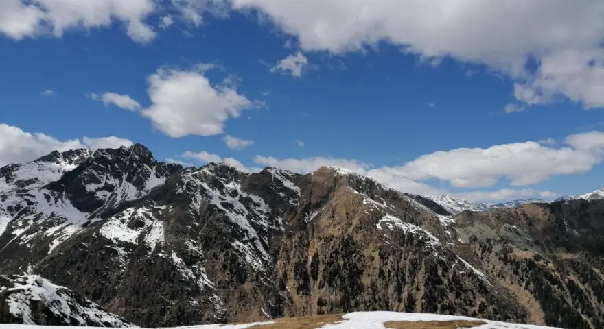 Cimon di Bolentina, un maestoso panorama montuoso con cime innevate e un cielo azzurro punteggiato di nuvole bianche.
