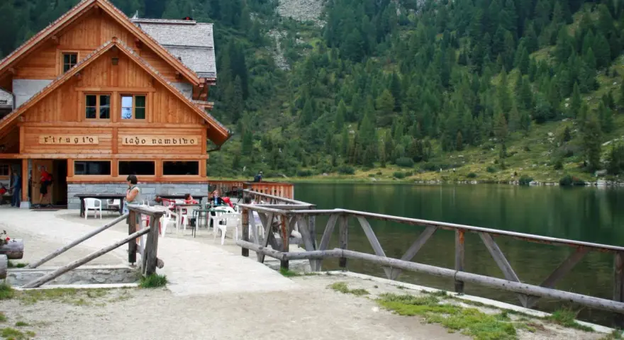 Rifugio sul lago nambino, con tavoli all'aperto e un bosco di conifere sullo sfondo.