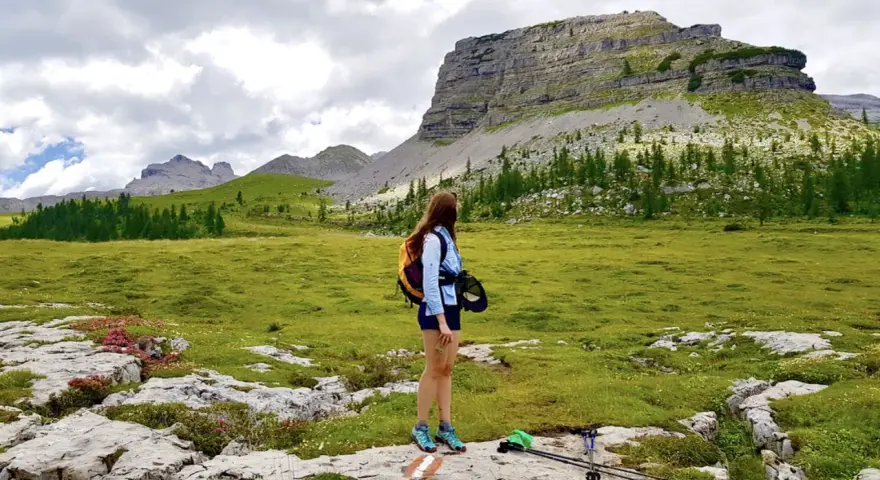 Ragazza con zaino ammira un paesaggio alpino con un imponente turrion basso.