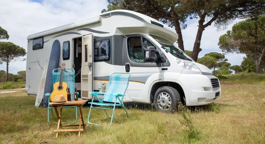 Un camper pronto per un tour in Trentino, con chitarra, cappello e sedie da campeggio in un prato verde.