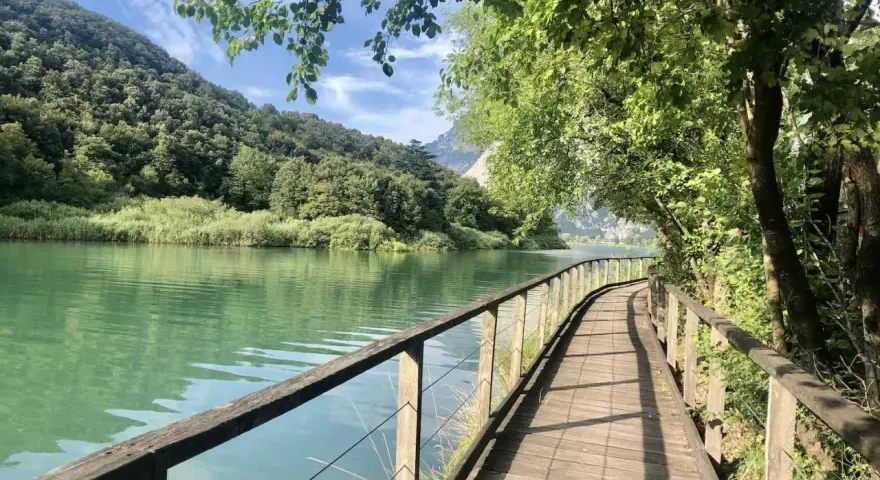 Sentiero in legno lungo il lago di Toblino, con montagne verdi sullo sfondo. Ideale per scoprire come arrivare.