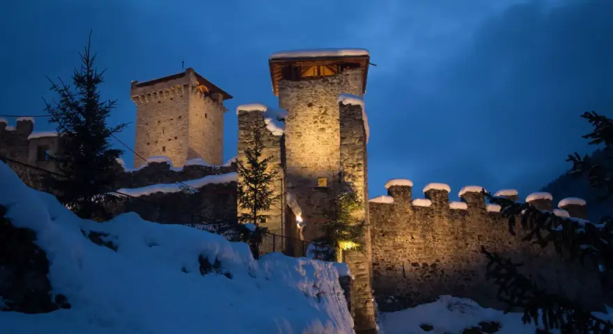 Castello innevato illuminato di notte, con alberi di Natale e luci che ricordano i mercatini di Natale di Ossana.