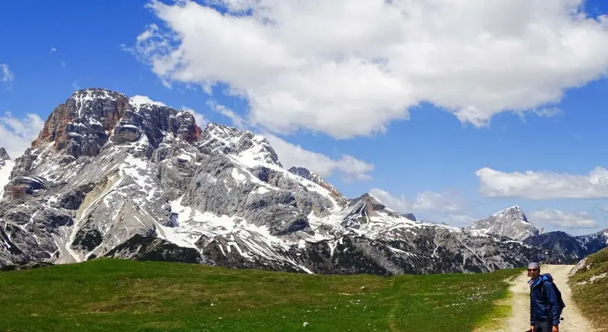 Un escursionista si ferma su un sentiero di montagna, con imponenti vette innevate sullo sfondo. Perfetti percorsi per camminare.