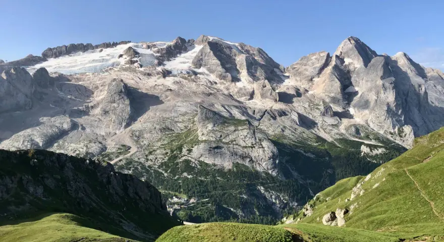 Vette innevate del Viel del Pan si stagliano maestose su un paesaggio alpino verdeggiante, con un piccolo borgo incastonato tra i boschi.