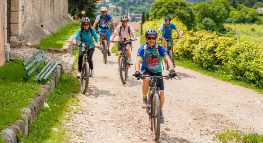 Gruppo di ciclisti su sentiero sterrato, godendosi gli eventi Trentino in un paesaggio verdeggiante.