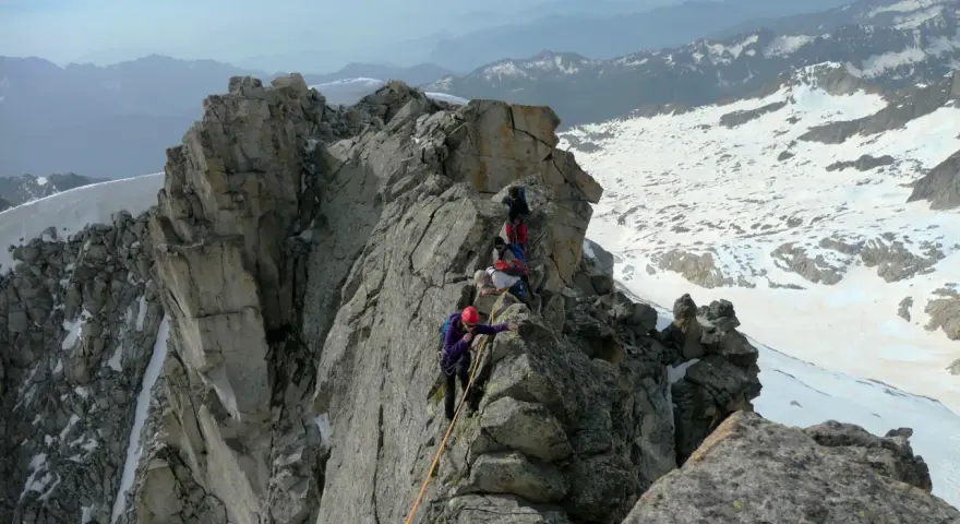 Alpinisti in cordata affrontano un crinale roccioso innevato, con la **cima Presanella** sullo sfondo.
