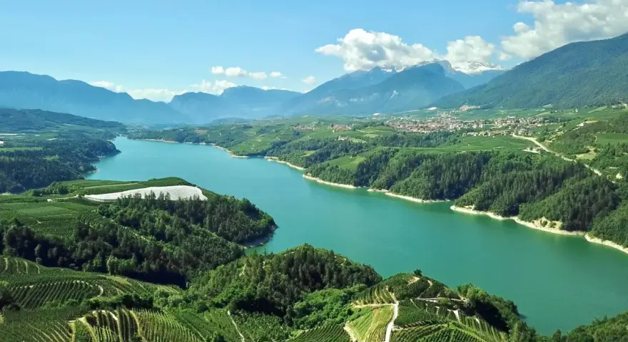 Panoramica mozzafiato del lago di Santa Giustina, circondato da verdi colline coltivate e montagne imponenti.