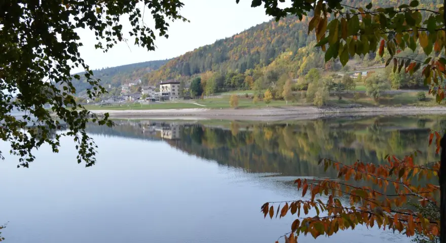 Autunno a Baselga di Pinè: il lago riflette le case e i boschi colorati. Cosa vedere in questo incantevole borgo trentino.
