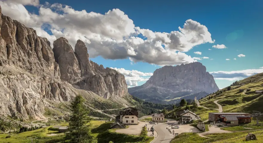 Panorami mozzafiato al Passo Gardena, con imponenti vette rocciose e un'altitudine che toglie il fiato. Case e strade si snodano tra i verdi pendii.