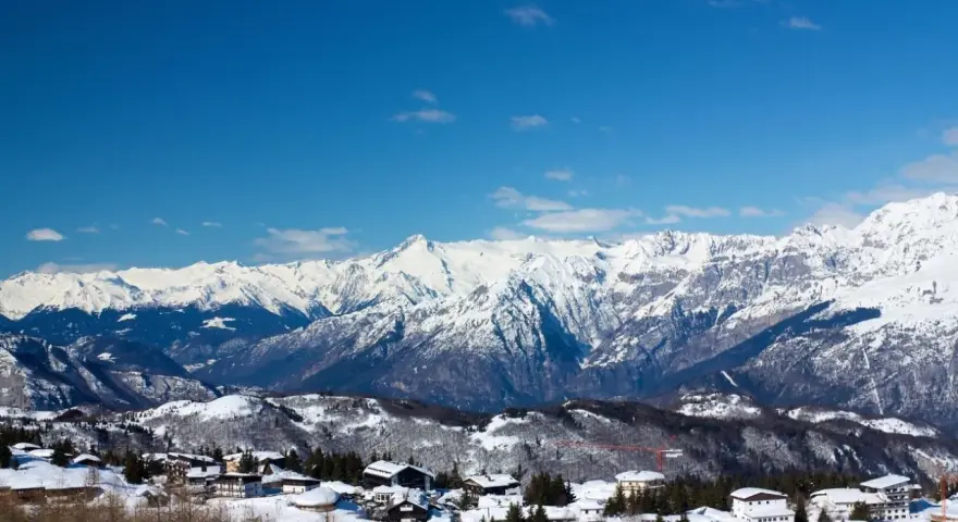 Paesaggio invernale con case innevate e montagne maestose sullo sfondo, un incantevole scenario al Passo Bondone.