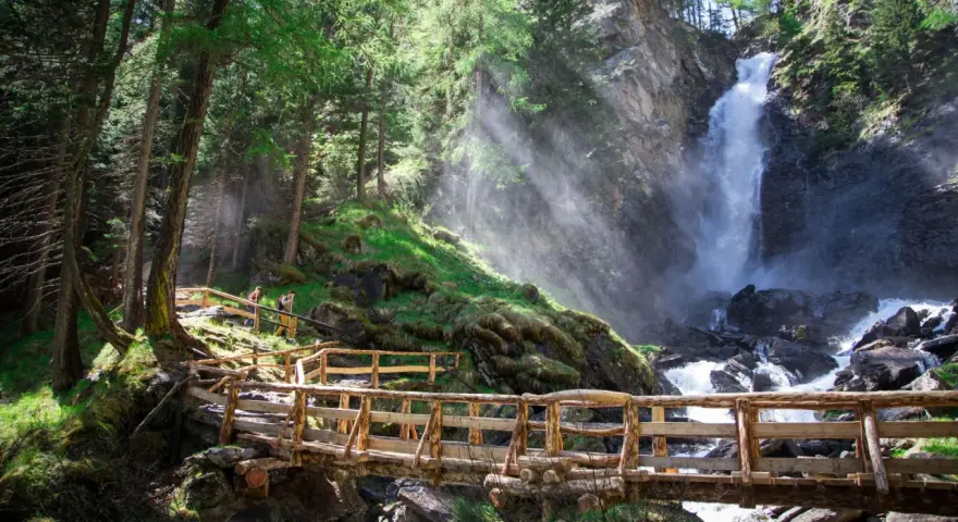 Sentiero in legno conduce alle maestose cascate Val di Sole, immerse in un bosco rigoglioso.