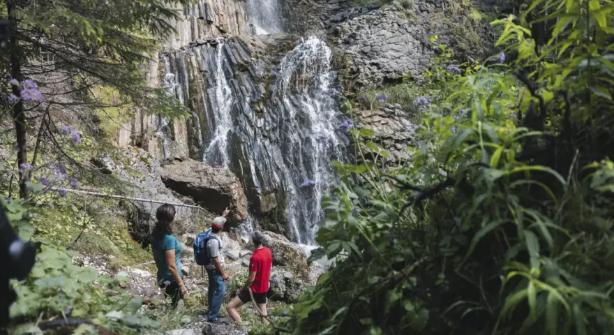 Escursionisti ammirano le spettacolari cascate schiavaneis, immerse nel verde e circondate da rocce basaltiche.