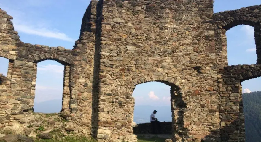 Rovine del castello di Altaguardia, con un uomo seduto che guarda il panorama.