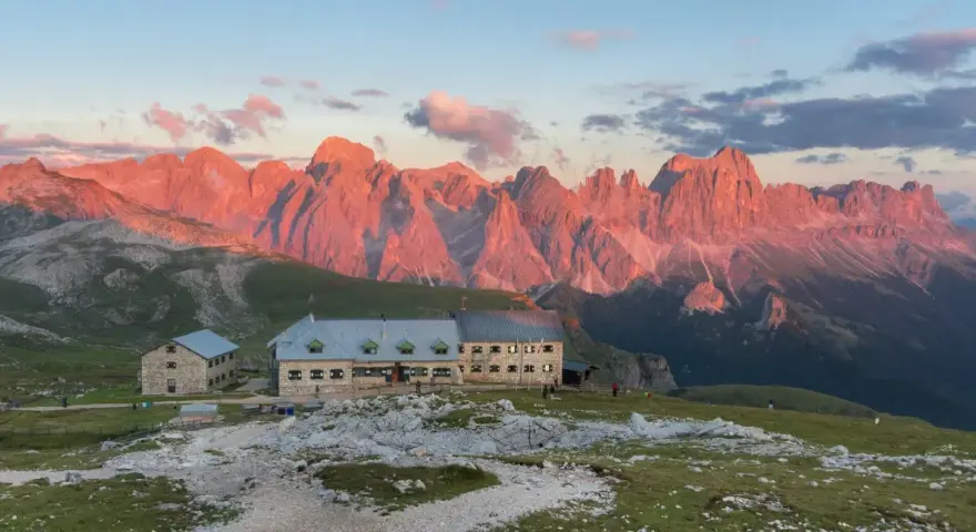 Rifugio sul **Monte Catinaccio** illuminato dal tramonto, con le vette rocciose che si tingono di rosa.