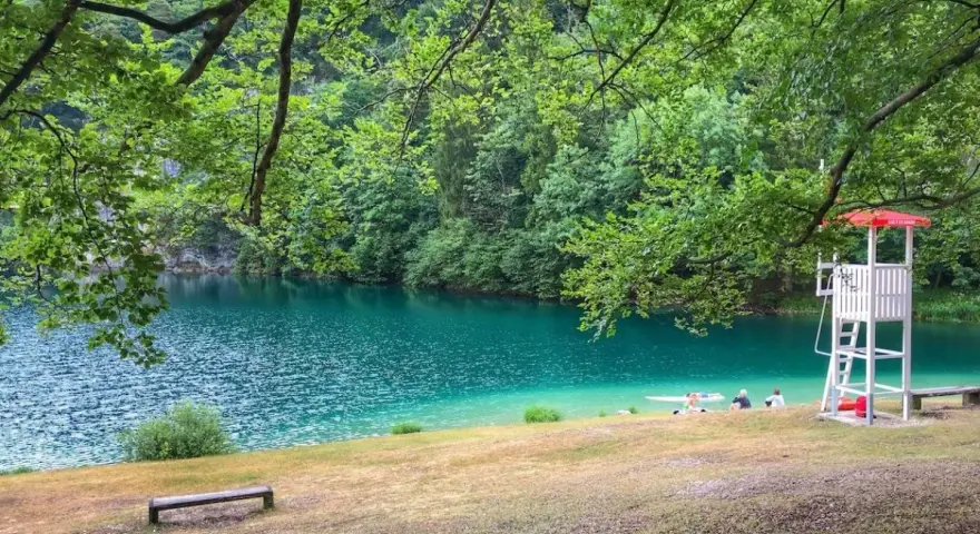 Rilassante **lago Lamar** con acque turchesi, bagnanti e torretta di salvataggio sotto alberi verdi.