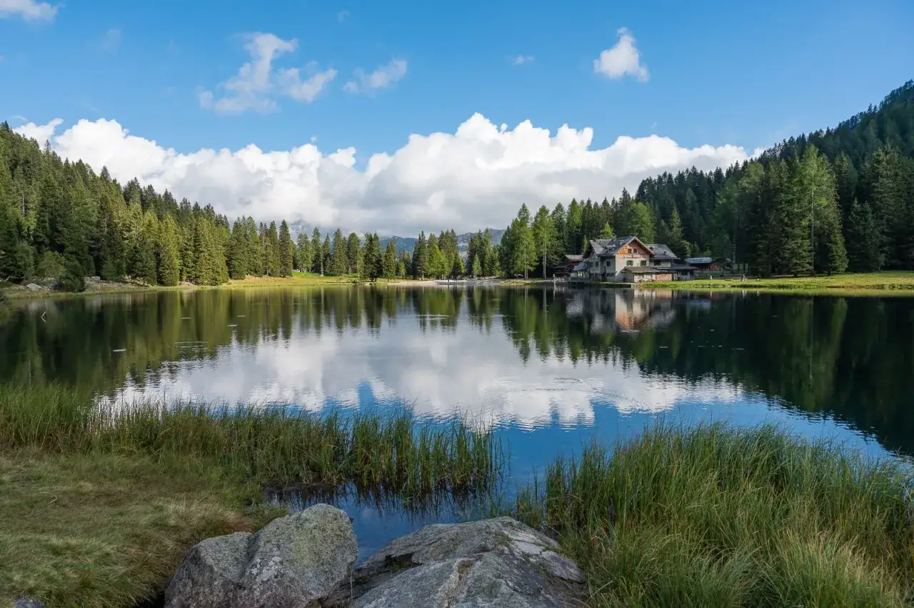 Lago alpino tranquillo nella piana di Nambino, con riflessi di cielo e boschi.